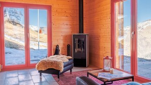 Un chalet confortable avec un grand lit, une cheminée et une vue sur un paysage enneigé, visible à travers les portes vitrées.