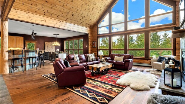 A spacious living room with a large wooden ceiling, a fireplace, and a view of the outdoors through large windows.