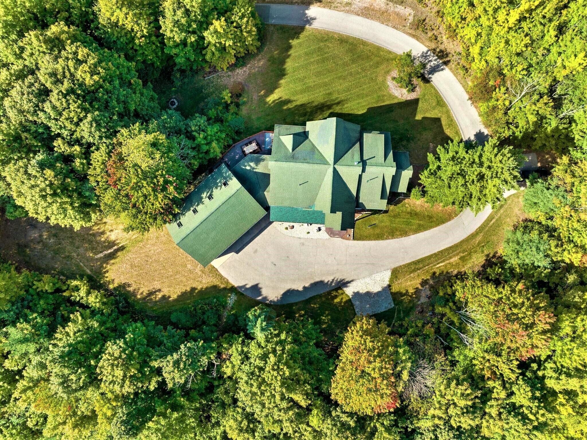 Une vue aérienne d’une maison entourée d’arbres denses, avec une allée sinueuse menant à l’entrée.