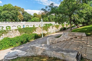 Stroll through the serene park to the historic building with arched windows, surrounded by lush greenery.