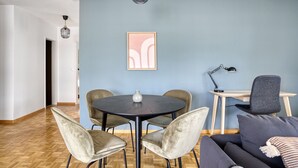 Una sala de estar moderna con una mesa redonda, cuatro sillas, un sofá, un escritorio con una silla y una obra de arte enmarcada en la pared.