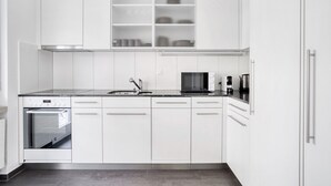 Una cocina moderna con armarios blancos, horno empotrado, microondas y cafetera.