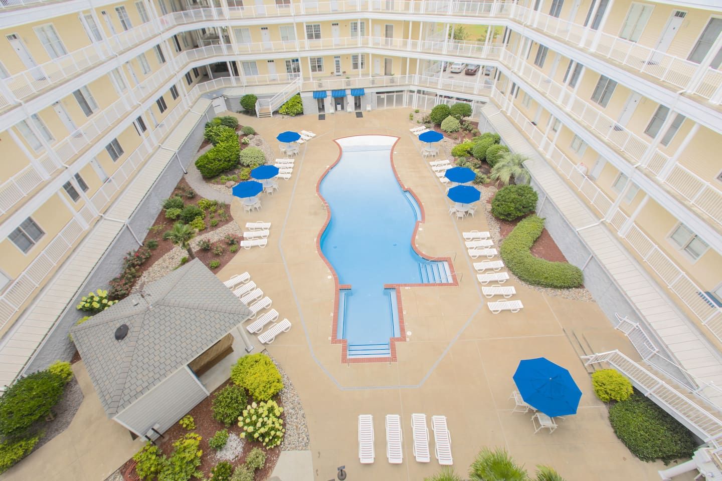 A multi-story hotel with a central swimming pool, outdoor seating, and a landscaped garden.