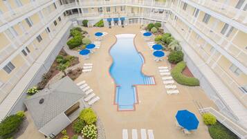 A multi-story hotel with a central swimming pool, outdoor seating, and a landscaped garden.