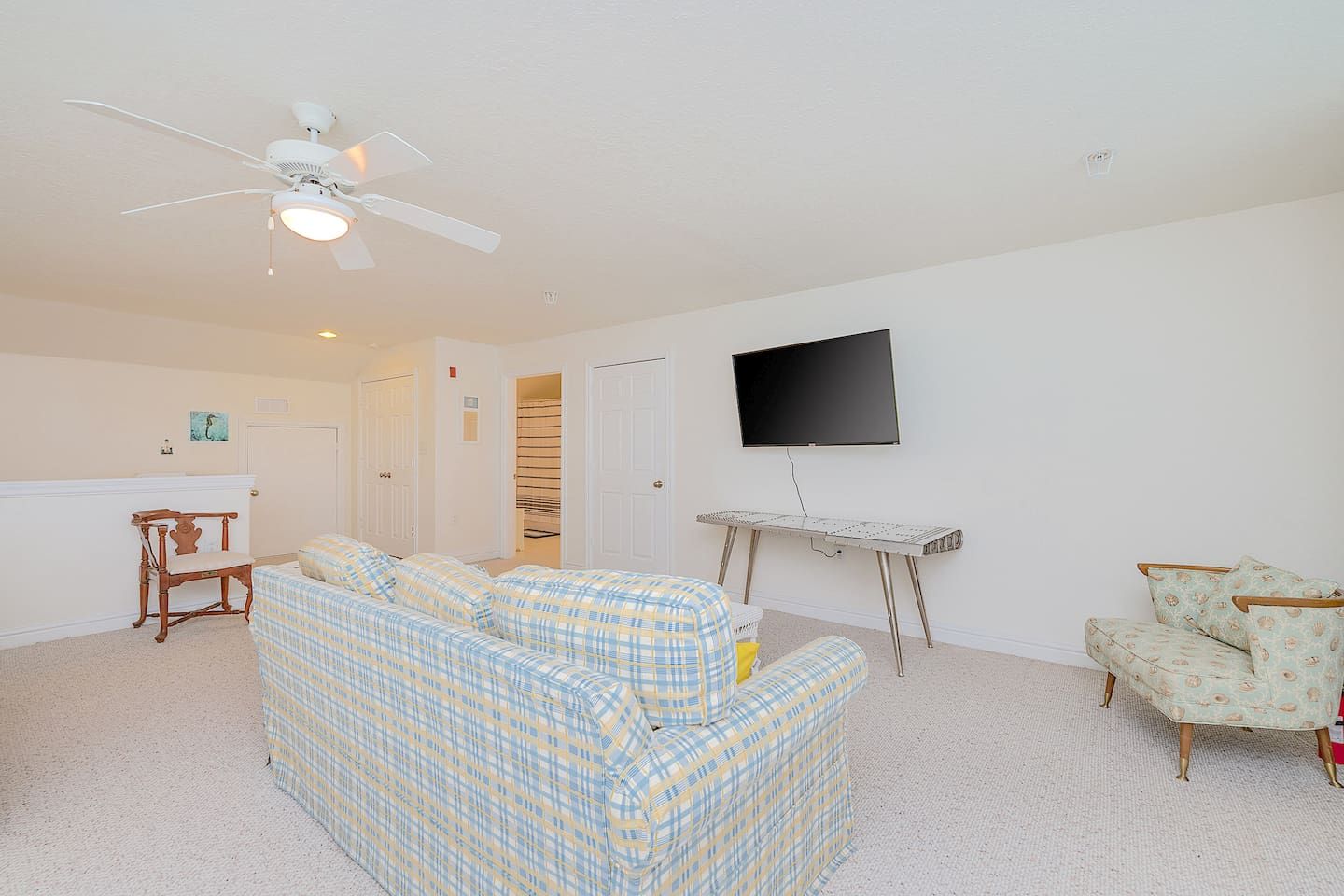 A living room with a ceiling fan, a television mounted on the wall, a patterned sofa, a small table, and a patterned armchair.
