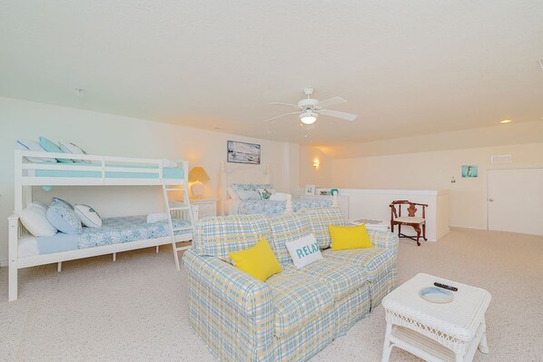 A bedroom with bunk beds, a sofa, a chair, a small table, and a ceiling fan.