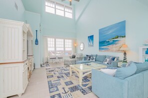 Un salon spacieux avec une grande fenêtre, un tableau représentant une plage et un meuble blanc.