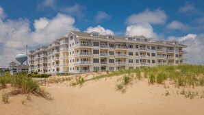 Un hotel de varios pisos con balcones, situado en una playa de arena con dunas.