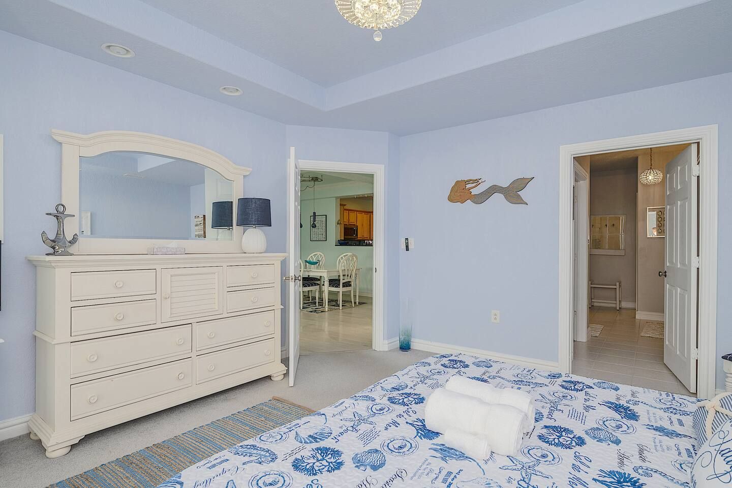 Een slaapkamer met een bed, een dressoir en een spiegel. Deur naar een andere kamer.