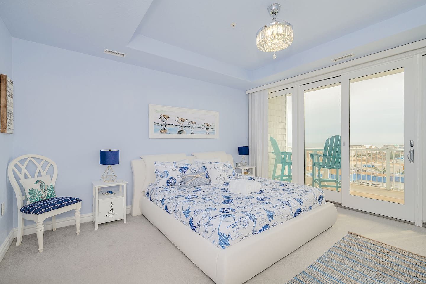 Een slaapkamer met een groot bed, twee nachtkastjes, een stoel, een kroonluchter en uitzicht door een schuifdeur.