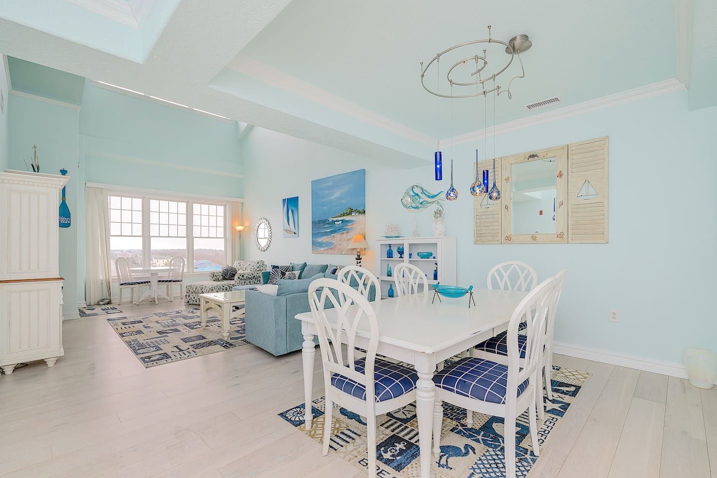 A spacious living area with a dining table, white chairs, and a blue sofa.