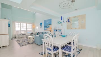A spacious living area with a dining table, white chairs, and a blue sofa.