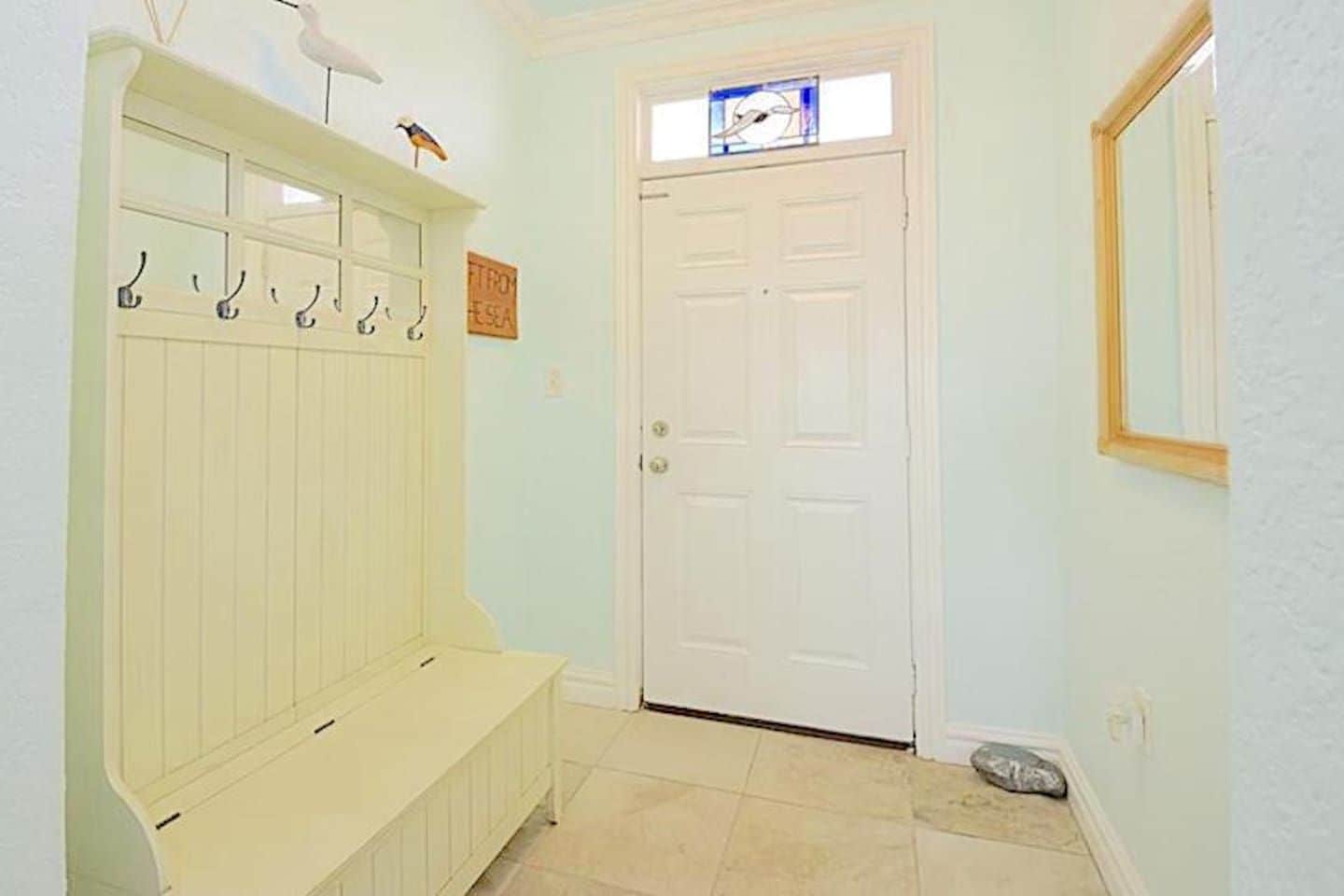 Un pasillo con una puerta blanca, un banco y un perchero con ganchos.
