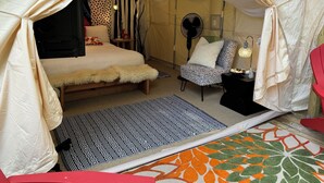 Une chambre confortable aménagée comme une tente, avec un lit, une chaise et une petite table dotée d’une lampe.