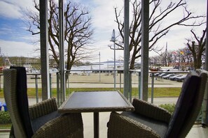 A covered outdoor seating area with a table and chairs, overlooking a parking lot and a large building. - Vacation apartment near the harbor with sea view - Hafenresidenz Lauterbach FeWo 2-2 - (Putbus)