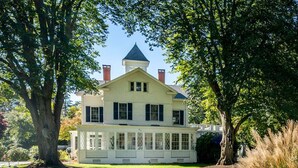 A large, two-story house with a wrap-around porch and a tower with chimneys. - Center Of It All: 454-Cv  Sea Captain's Estate with Heated Pool and Pickle Ball Court (Centerville)