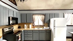 Une cuisine de taille réduite avec des meubles gris, un micro-ondes noir, un réfrigérateur blanc et un plan de travail en bois.