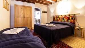 A room with two beds, wooden beams on the ceiling, a wooden door, and a colorful tapestry on the wall. - Apartment Campaniel Veneziacentopercento (Venezia)