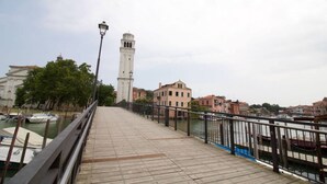 Una passera de fusta amb un fanal, una torre blanca i edificis al costat d'un canal.