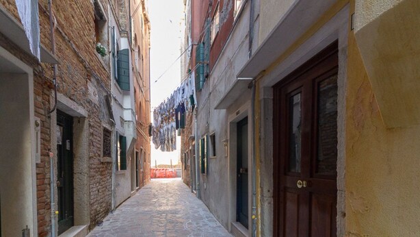 Un carrer estret amb paviment de pedra, flanquejat per edificis amb portes i persianes de fusta.