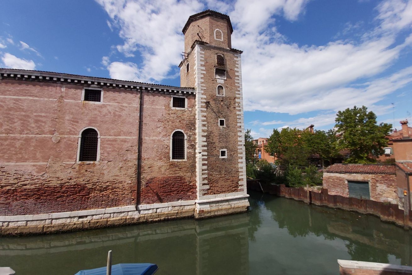A historic building with a tall tower, a canal in front, and a clear sky.