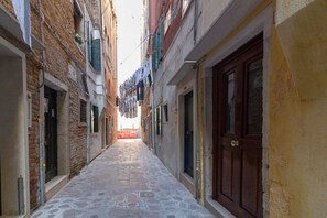 Un stretto vicolo con pavimentazione in pietra, delimitato da edifici con porte e persiane in legno.
