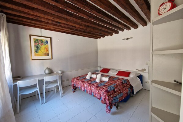 A bedroom with a bed, a desk, two chairs, a painting on the wall, and a clock on the wall. - Ca' Riello Apartment - Veneziacentopercento (Venezia)