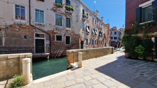 A narrow canal with buildings on either side, a stone pathway, and a clear sky. - Ca' Riello Apartment - Veneziacentopercento (Venezia)