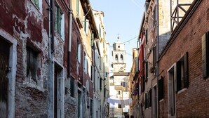 A narrow street with old buildings, a bell tower in the distance, and laundry hanging between the buildings. - Picenin Apartment - Veneziacentopercento (Venezia)