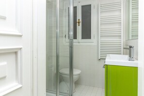 Un baño con cabina de ducha de vidrio, inodoro y lavamanos con gabinete verde.