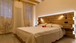 Un dormitorio con cabecera de madera, una cama con cubrecama blanco y una ventana con cortinas traslúcidas.