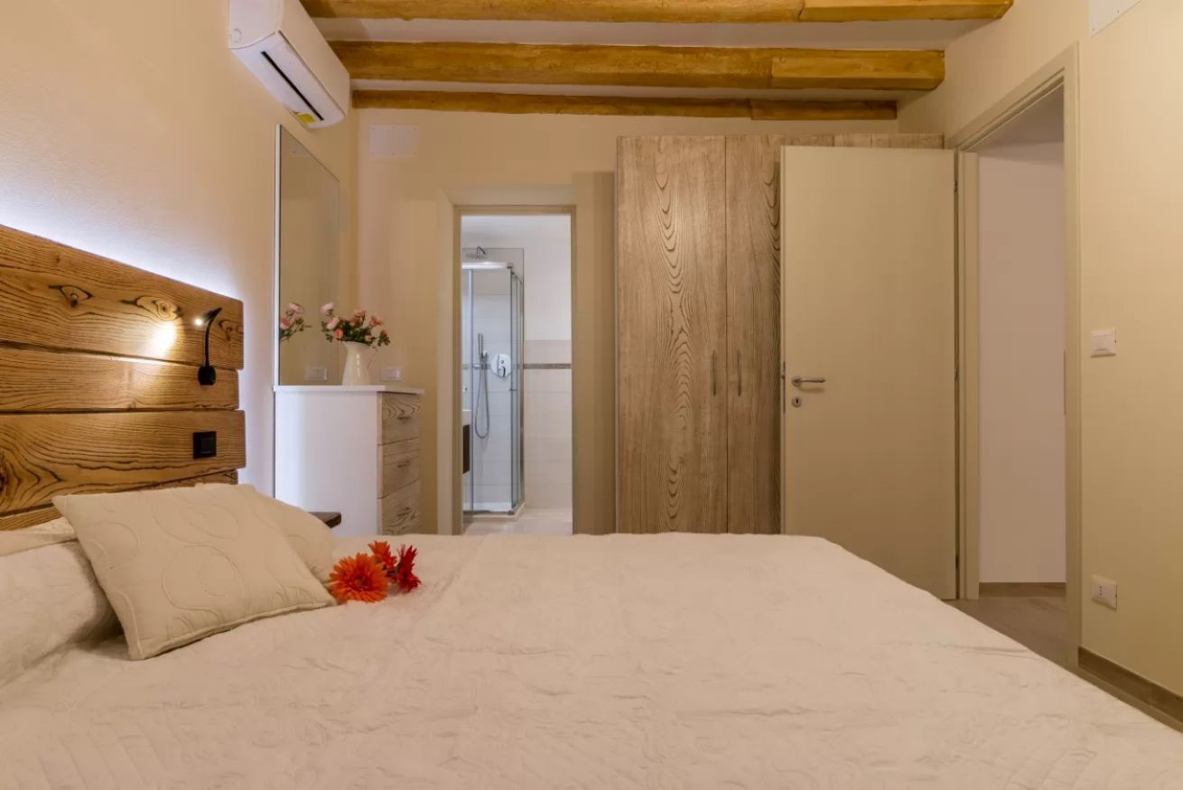A bedroom with a wooden headboard, a bed with white bedding, a nightstand with a vase of flowers, and a wooden wardrobe.