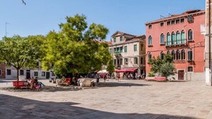 Una plaza pública con adoquines de piedra, árboles y edificios históricos con ventanales arqueados.