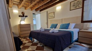 Ein Schlafzimmer mit Schachbrettfußboden, einem Bett mit blau-weißer Bettwäsche, einem hölzernen Schminktisch und einer Holzzieldecke.