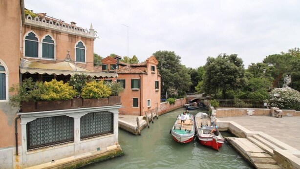 Un canal estrecho con barcos amarrados, rodeado de edificios históricos con ventanas arqueadas y un puente al fondo.