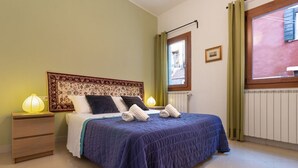 Un dormitorio con cama, dos mesitas de noche, una ventana con cortinas y un radiador.