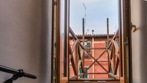 Vista a través de una ventana con marco de madera y estructura metálica de soporte, que da a un edificio rojo con tejado de tejas y una antena parabólica.