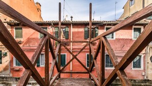 Una escalera de madera que sube hacia un edificio con fachada roja y contraventanas verdes.