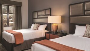 Una habitación de hotel con dos camas, una mesita de noche con lámpara y una ventana con cortinas.
