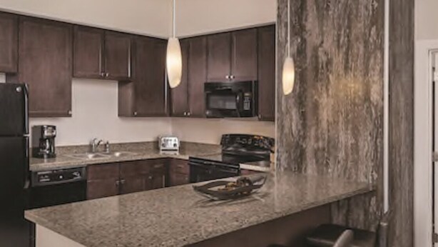 A kitchen with dark wooden cabinets, a granite countertop, a black refrigerator, a microwave, and a toaster.