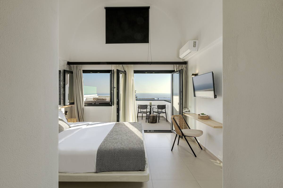 Une chambre d’hôtel moderne dotée d’un grand lit, d’un téléviseur fixé au mur et d’un balcon offrant une vue sur la mer.