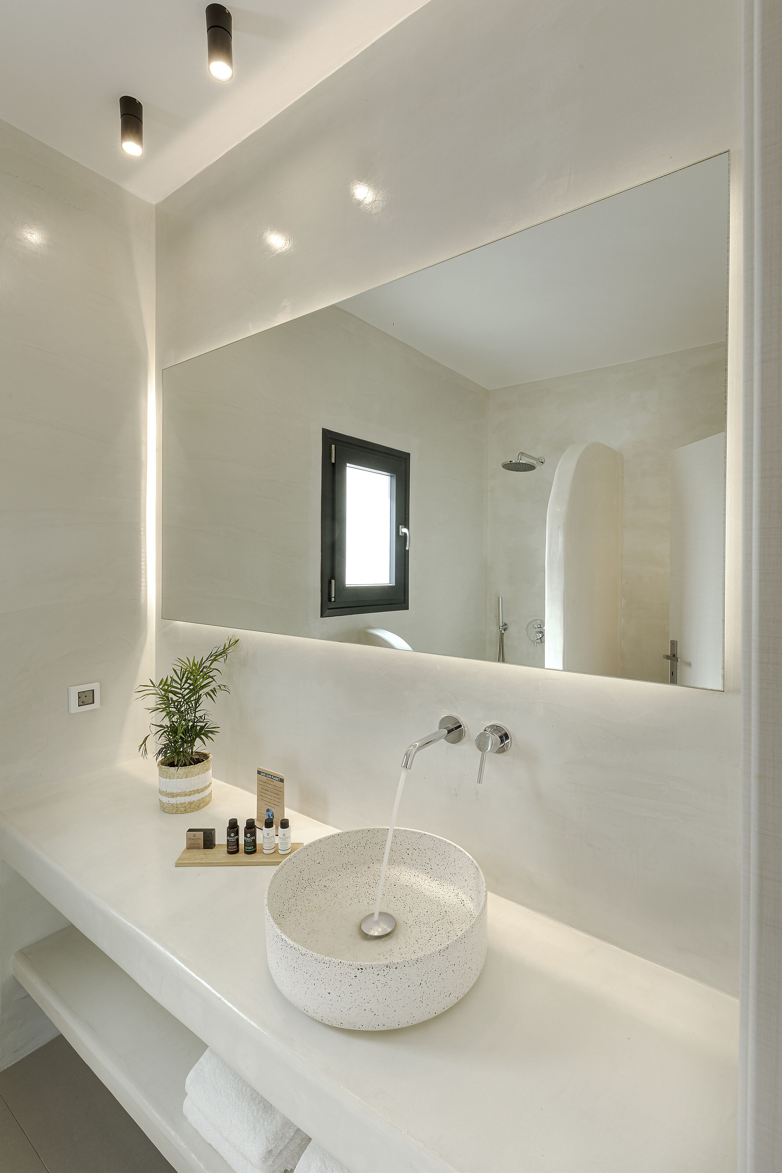 A modern bathroom with a large mirror, a round sink, and a potted plant.