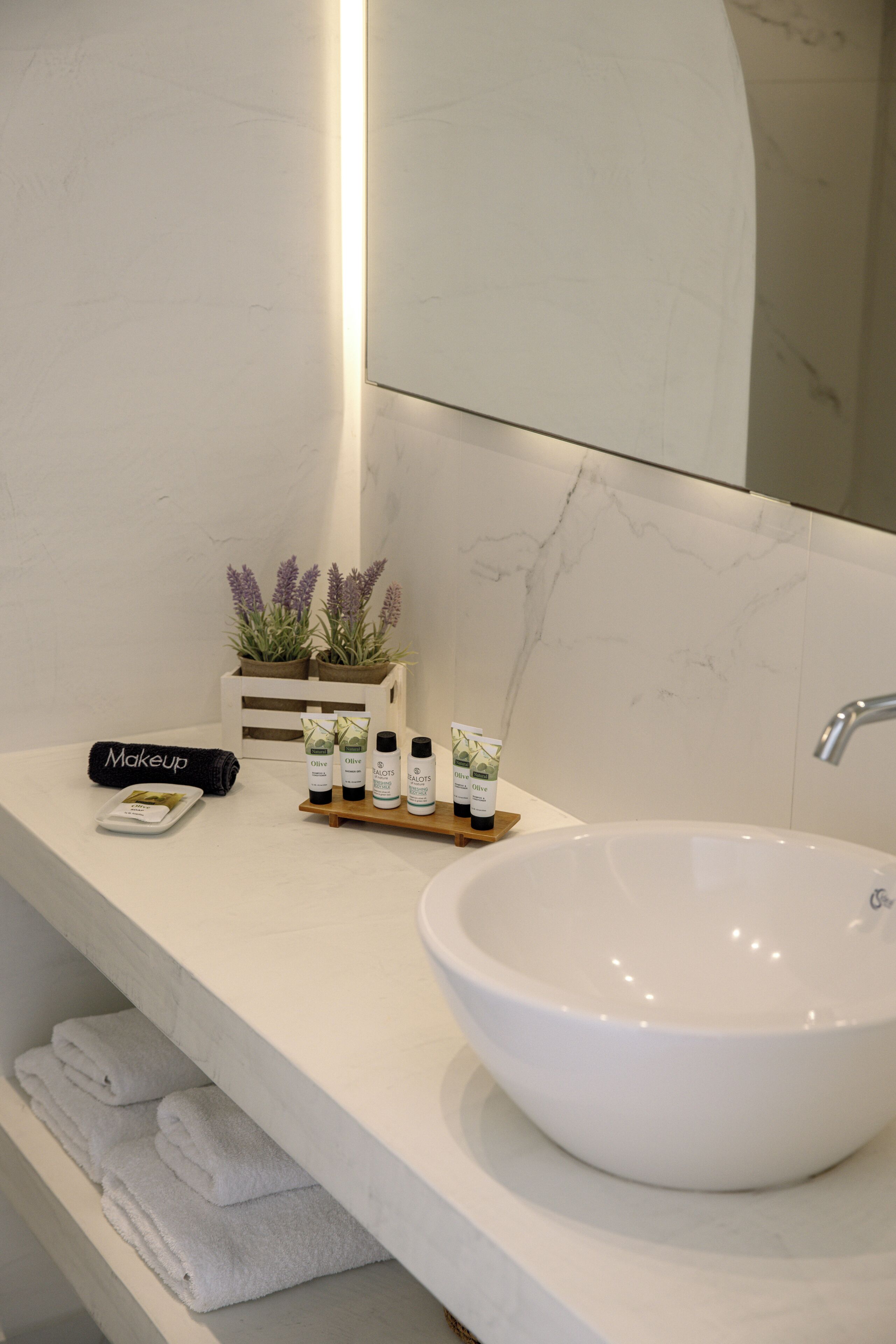 Une salle de bain avec un lavabo blanc, un miroir, un porte-serviettes et une étagère contenant des articles de toilette.