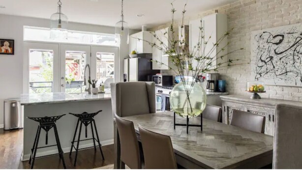 Una cocina moderna con una isla grande, taburetes de bar y un florero con ramas.