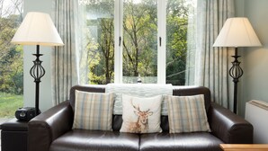 A cozy living room with a leather sofa, two lamps, and a window with curtains. - Cottage 420 - Clifden - sleeps 4 guests  in 2 bedrooms (Clifden)