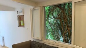 Una habitación con un banco de madera, un sofá gris y una ventana con vista a árboles.