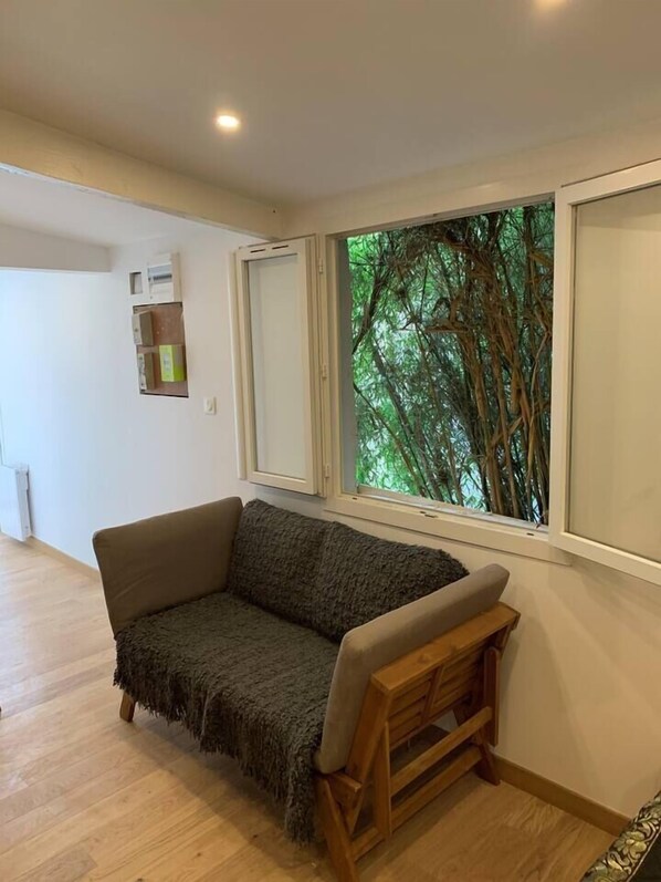 A room with a wooden bench, a grey sofa, and a window with a view of trees.