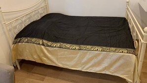 Una cama individual con una colcha negra y dorada en una habitación con cabecera y piecera de metal blanco.