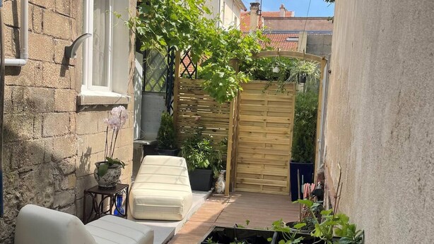Un patio exterior estrecho con cerca de madera, sofá blanco y plantas en macetas.