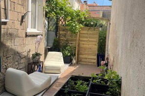 A narrow outdoor patio with a wooden fence, a white sofa, and potted plants.